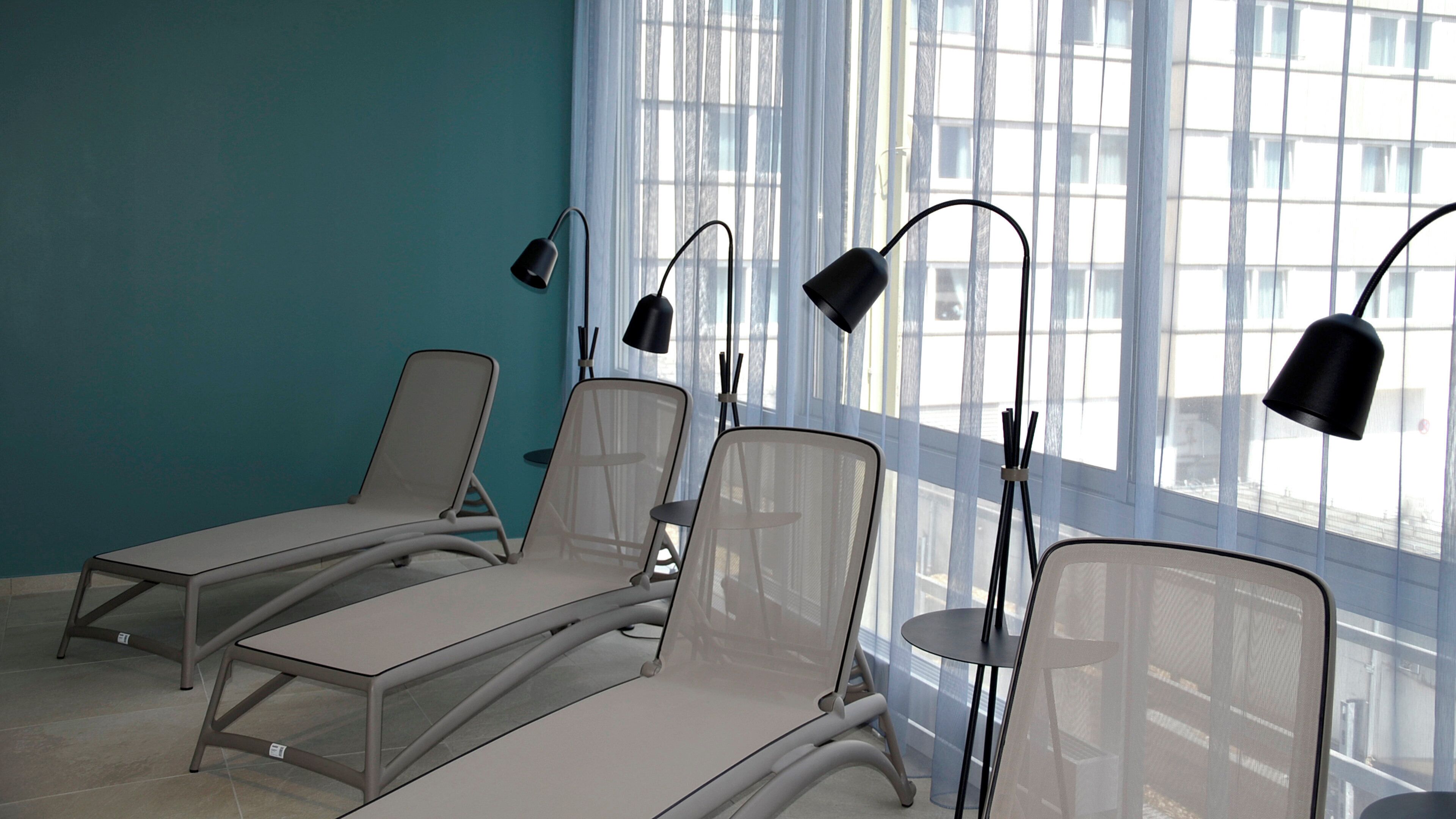 Uma área de espera com quatro poltronas reclináveis e duas luminárias de chão.