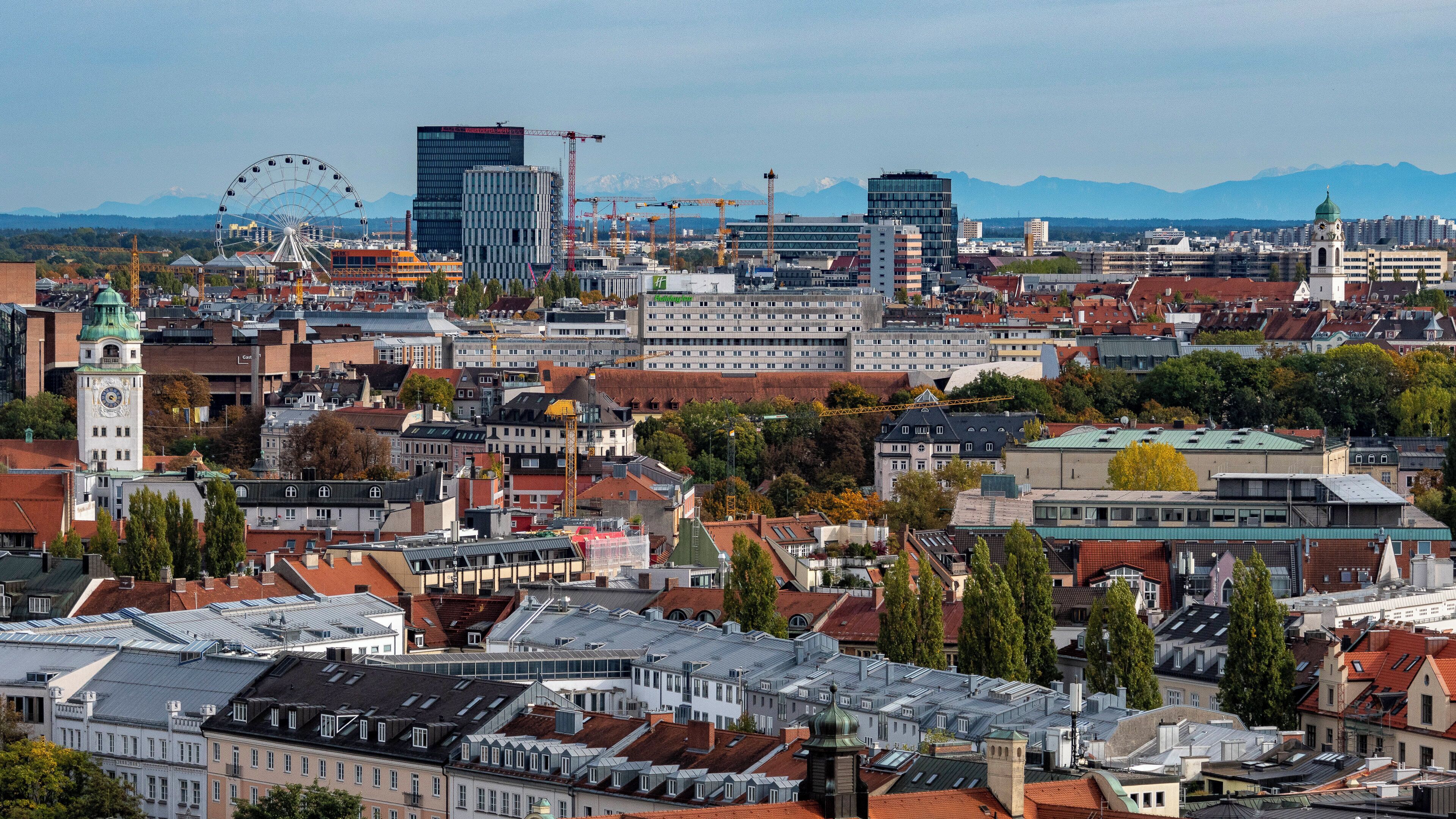 A cityscape with a mix of historic and modern buildings, including a prominent clock tower and a Ferris wheel in the background.
