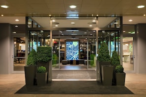 A hotel entrance with glass doors, a reception desk, and a seating area with a map display. - Holiday Inn Munich - City Centre by IHG (Munich)