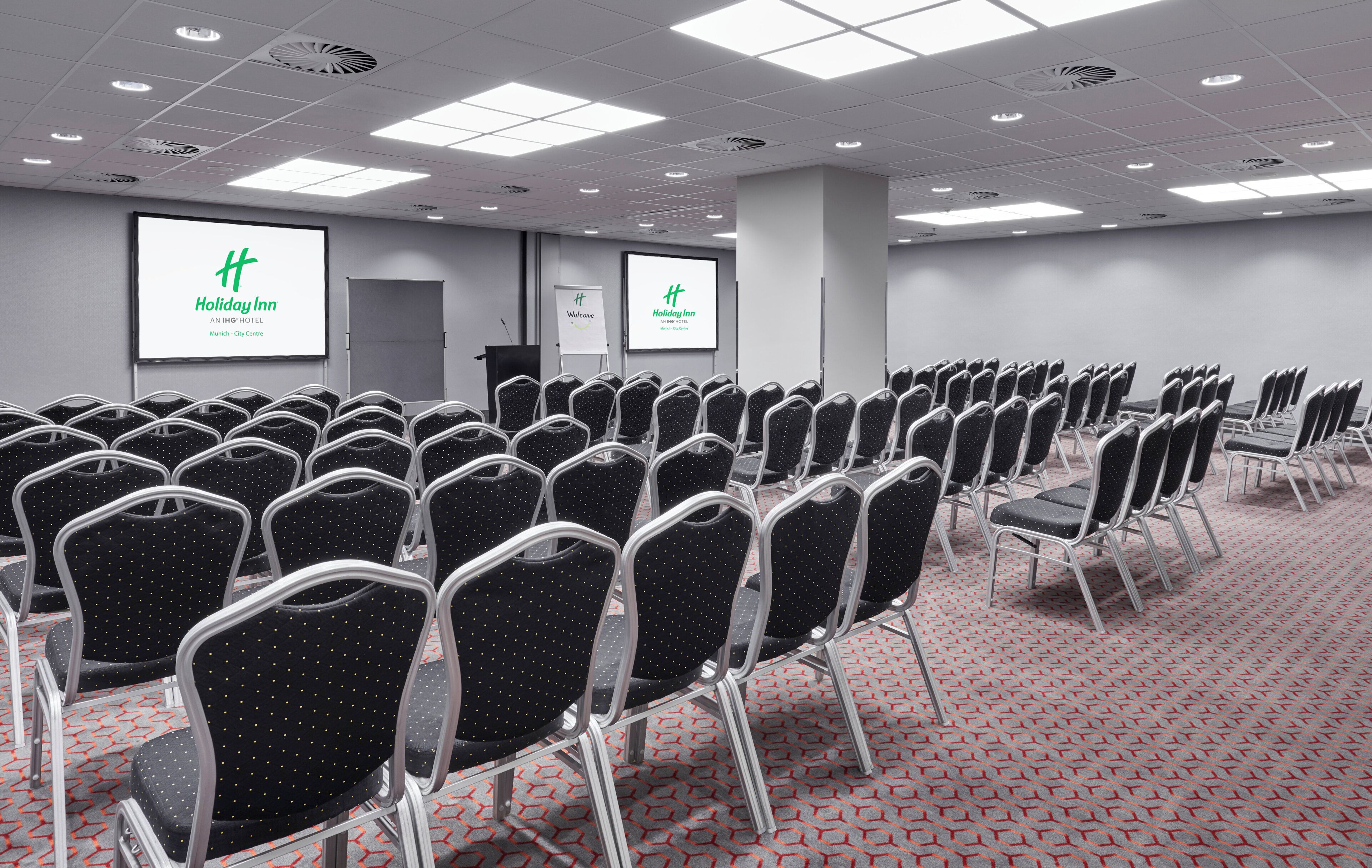 A conference room with rows of chairs, a podium, and two screens displaying the Holiday Inn logo.