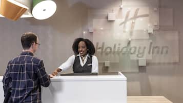 A Holiday Inn reception desk with a modern design, a nameplate, and a logo on the wall.