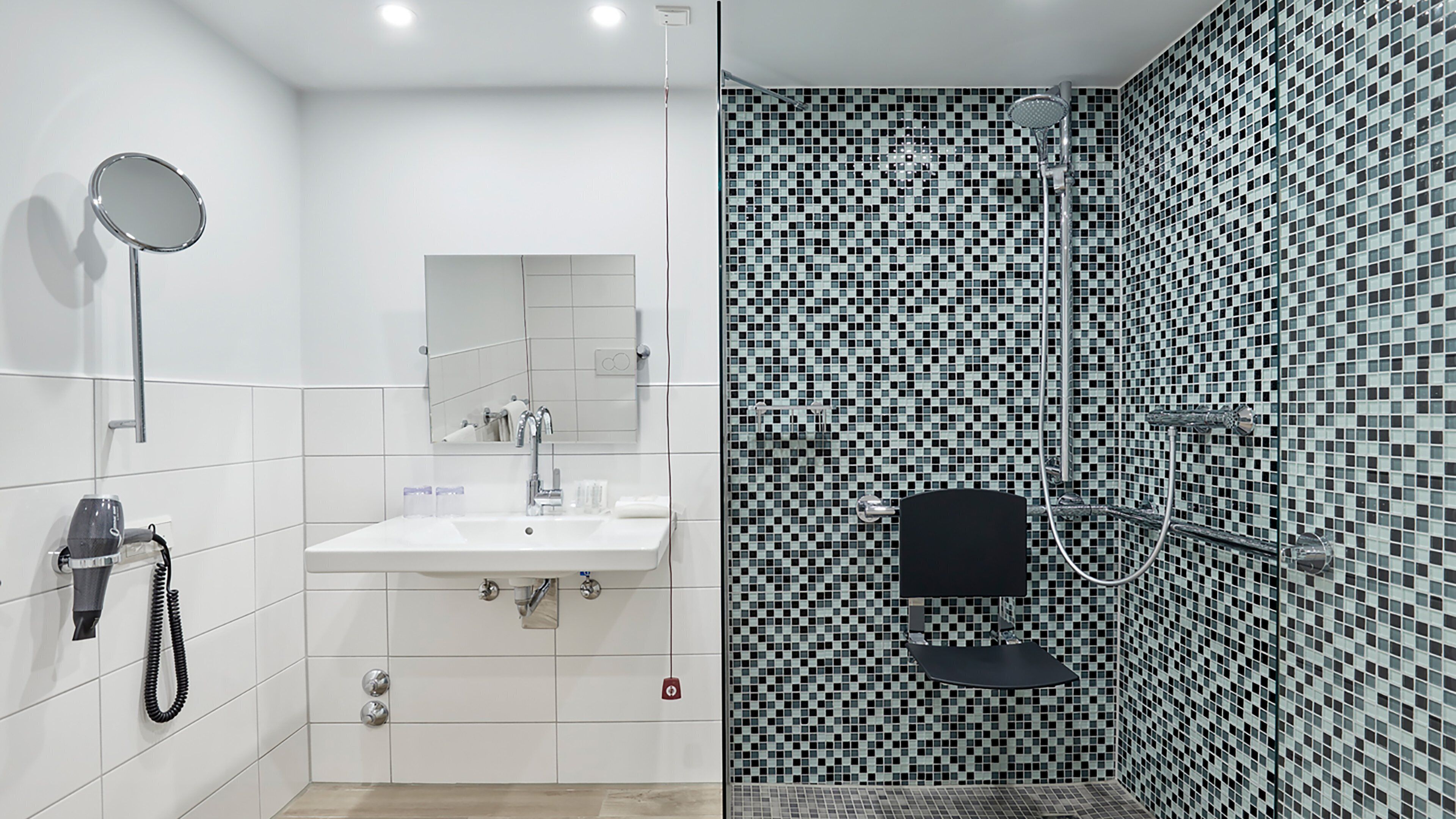 Un baño moderno con lavamanos blanco, espejo y zona de ducha con paredes de mosaico.