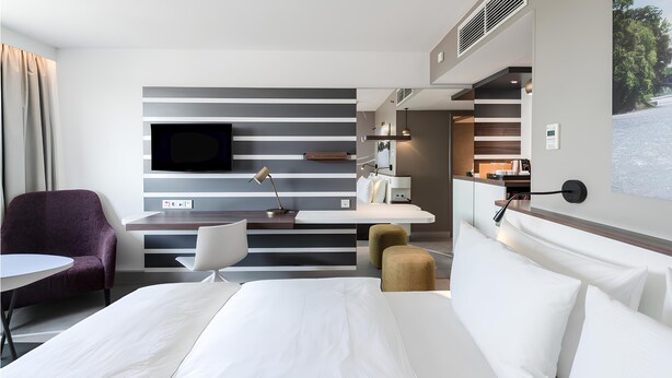 Una habitación de hotel moderna con una cama grande, un escritorio con televisor de pantalla plana, una silla y una mesita.