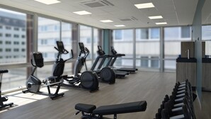 Un gimnasio moderno con máquinas de cardio, bancos de pesas y grandes ventanales con vistas a la ciudad.