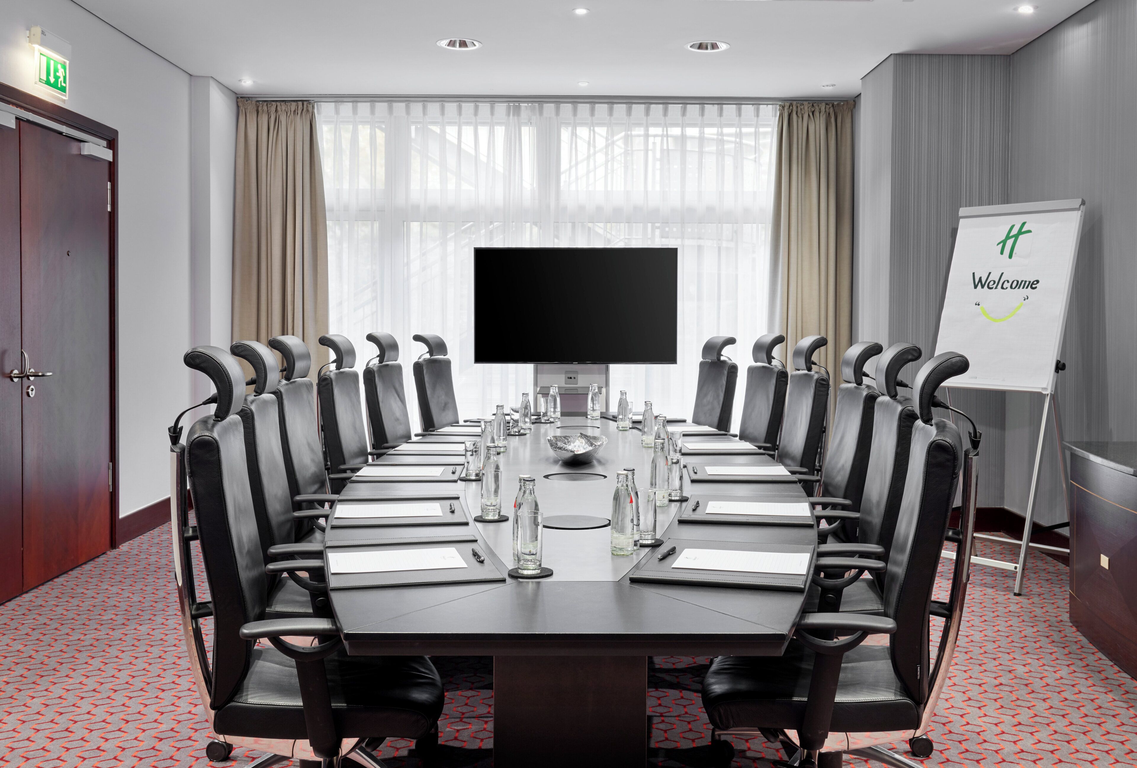 A conference room with a long table, chairs, a TV, and a whiteboard with a welcome message.