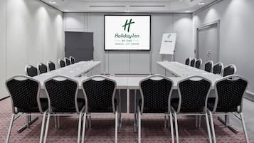 Un salón de conferencias con una larga mesa y sillas, una pantalla de proyector mostrando un logotipo, y un cartel de bienvenida.