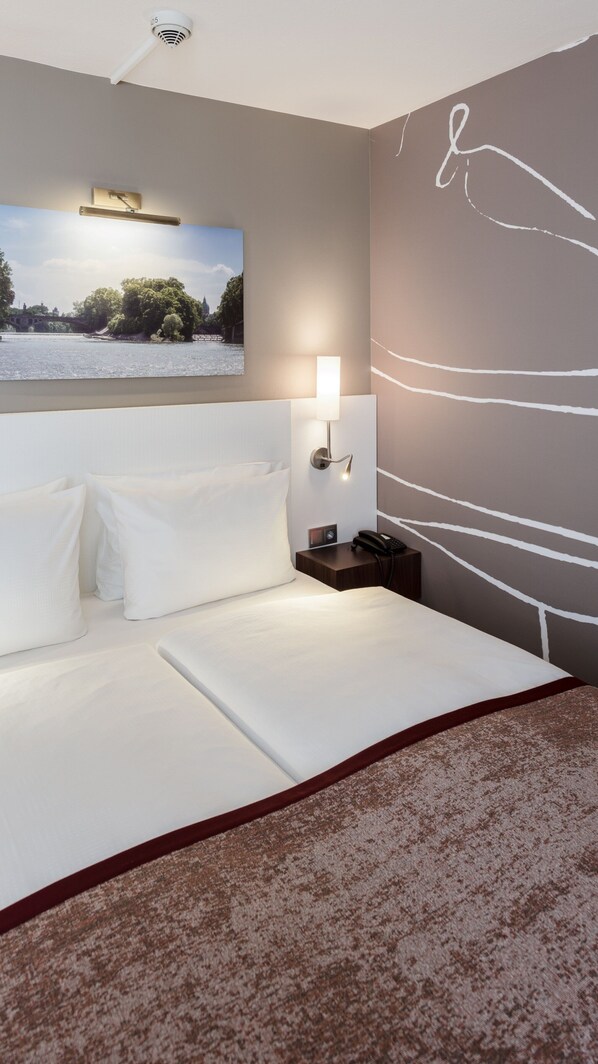 A hotel room with a large bed, a nightstand with a lamp, a phone, and a wall-mounted picture of a river scene.