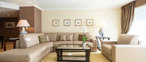 Una sala de estar con un sofá color beige, una mesa de centro de vidrio y una planta en maceta. Hay cuadros en la pared y una lámpara sobre una mesita.