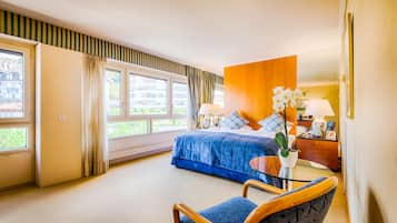 A hotel room with a bed, a chair, a small table, and a window with curtains.