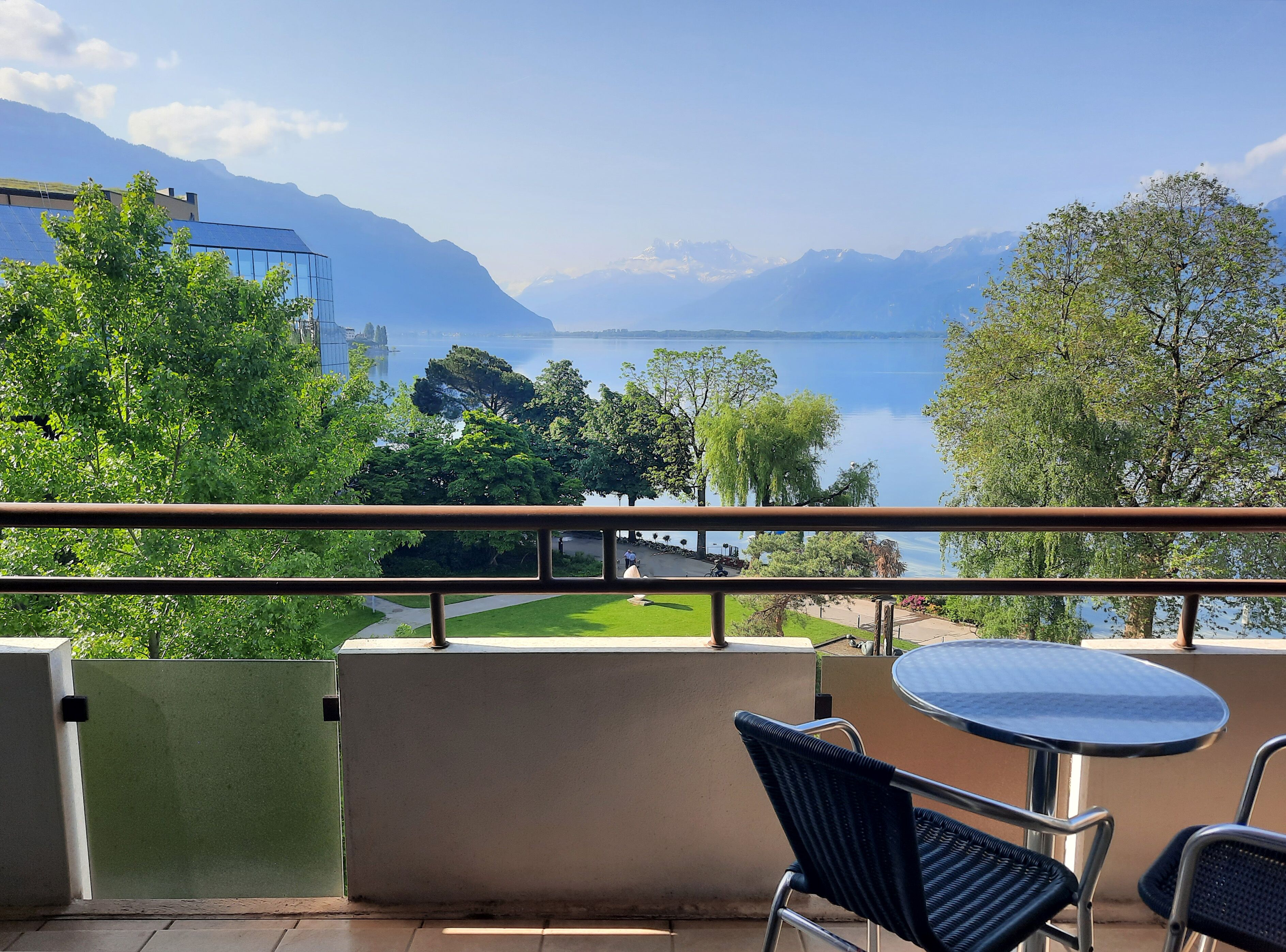 Varanda com vista para um lago e montanhas, com mesa e cadeiras.