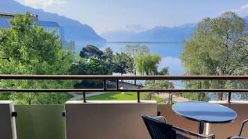 Varanda com vista para um lago e montanhas, com mesa e cadeiras.