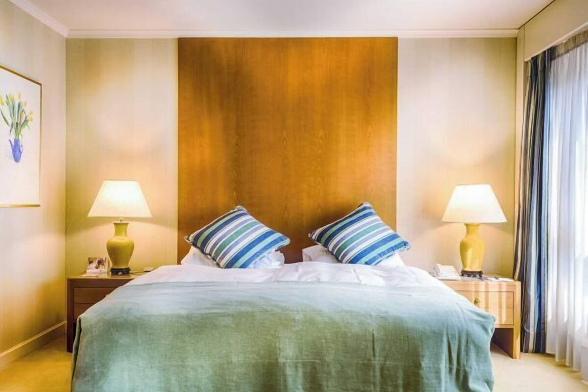 Una habitación de hotel con una cama grande, dos lámparas de noche, un cabecero de madera y un cuadro en la pared.
