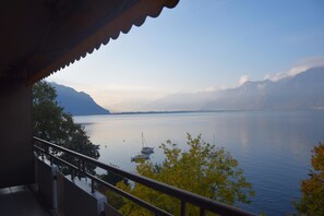 Un balcón con vistas a un lago tranquilo, barcos y montañas lejanas.