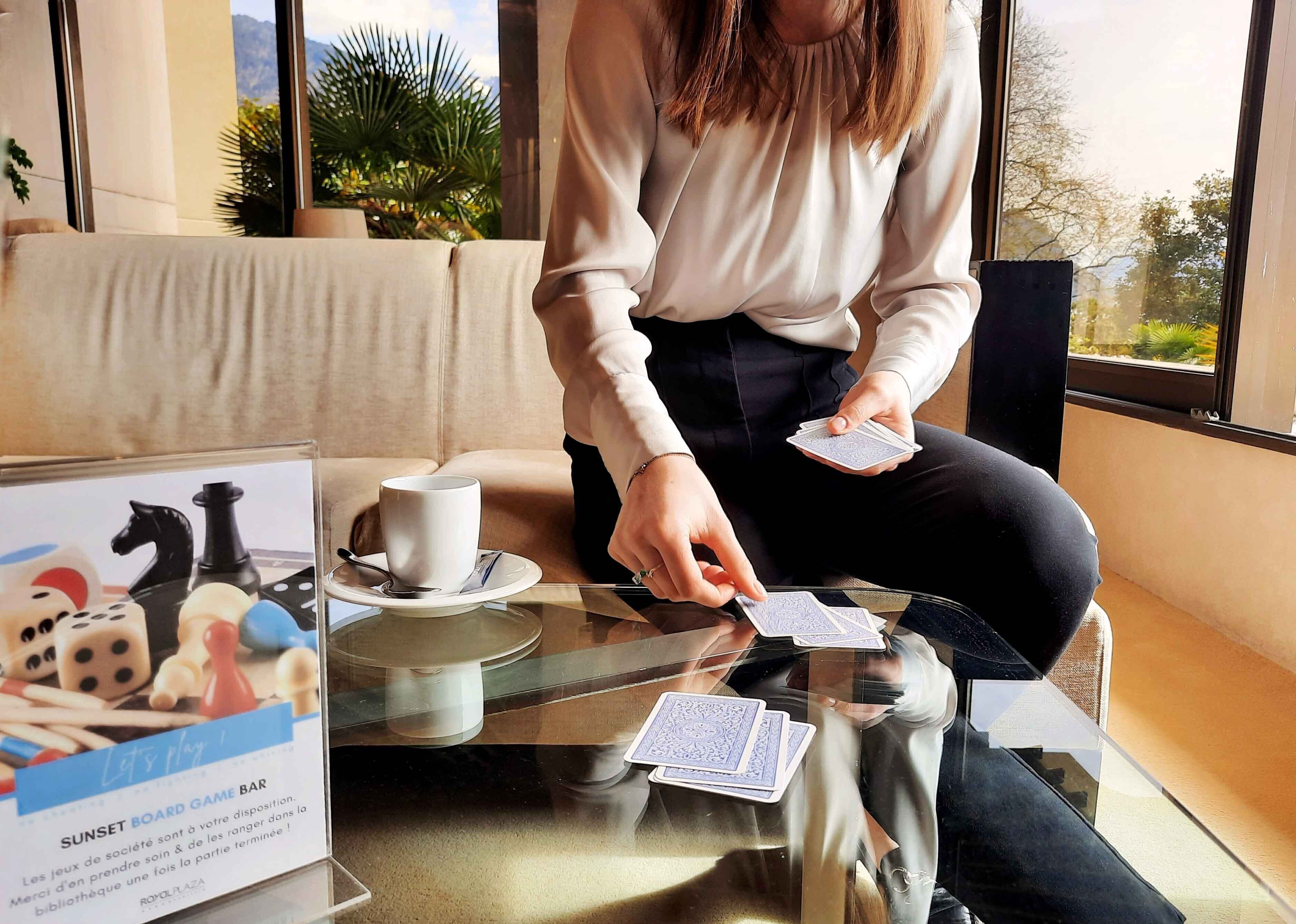 A person playing a card game at a table with a coffee cup and a board game set.