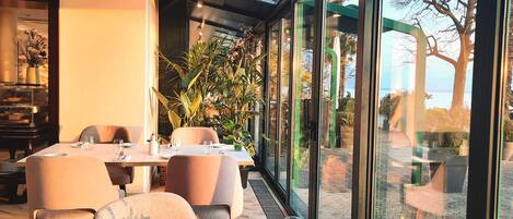 Un comedor con una mesa dispuesta para dos, ventanas amplias y plantas de interior.