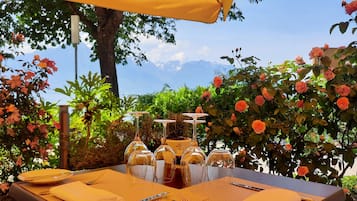An outdoor dining setup with a table set for four, surrounded by lush greenery and a clear sky.