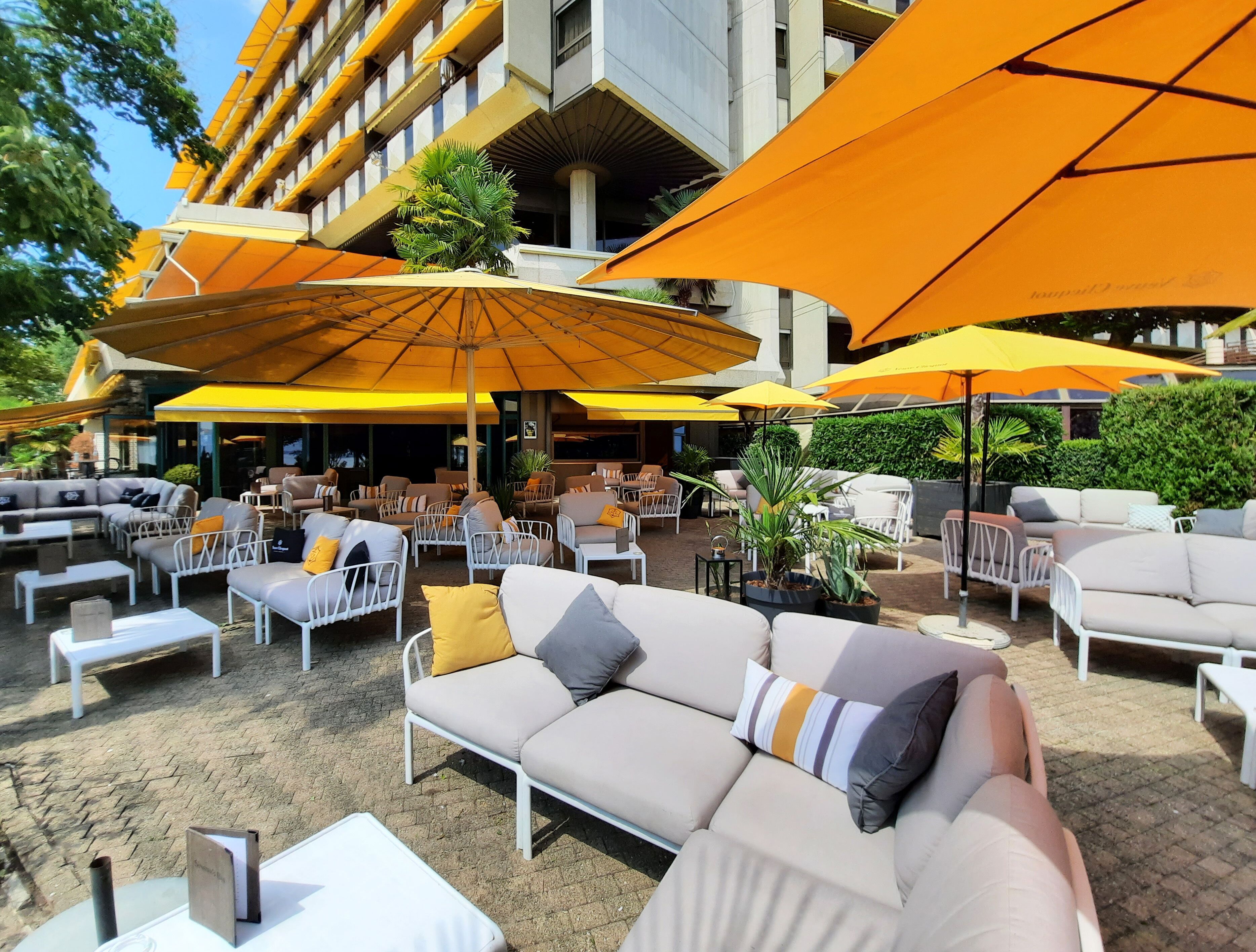 An outdoor seating area with multiple sofas and chairs, large yellow umbrellas, and potted plants.