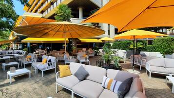 An outdoor seating area with multiple sofas and chairs, large yellow umbrellas, and potted plants.
