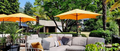 An outdoor seating area with a sofa and chairs, surrounded by potted plants and umbrellas.