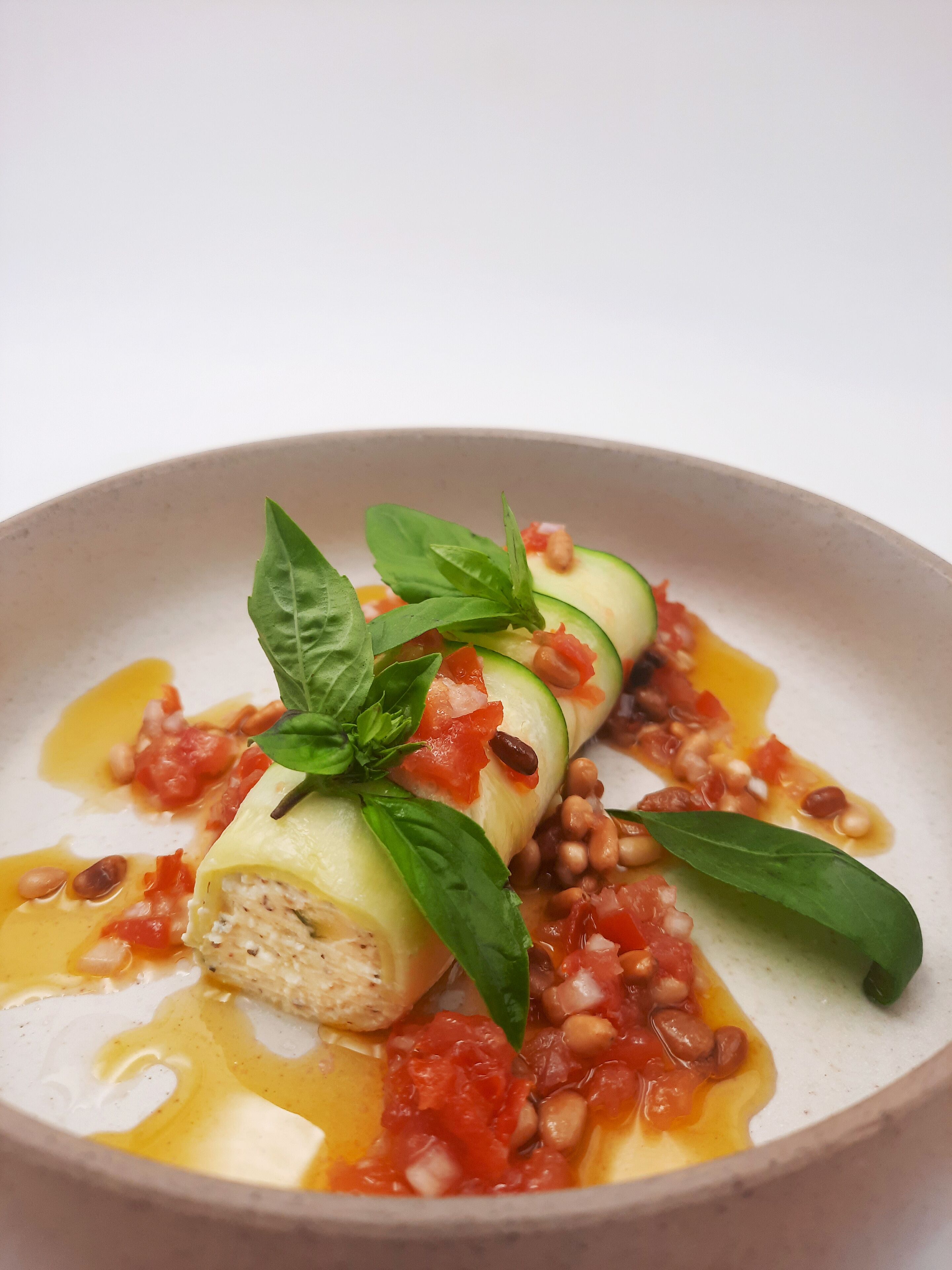 A dish with rolled vegetables, a basil leaf garnish, and a tomato-based sauce.