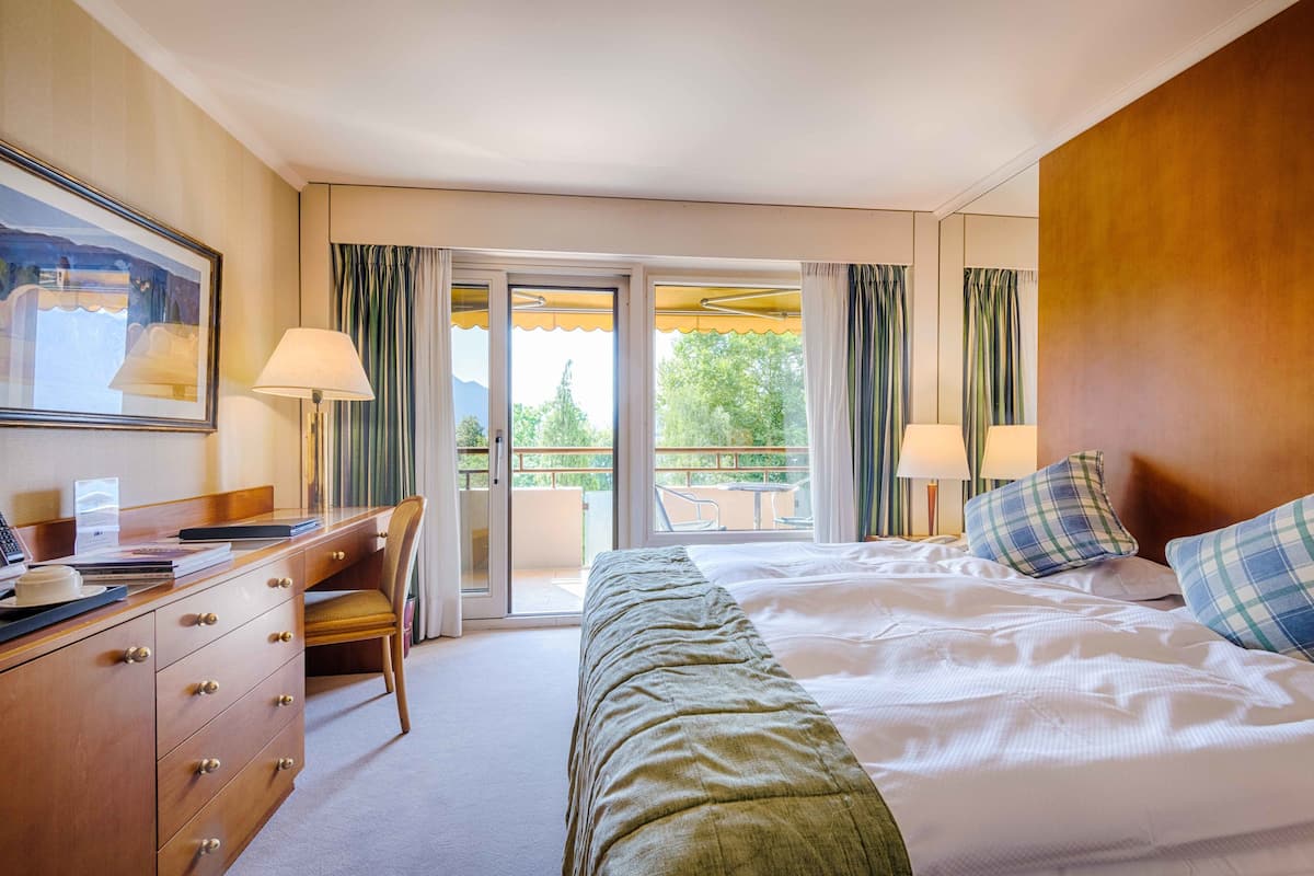 A hotel room with a bed, a desk, a chair, a lamp, and a view of the outdoors.