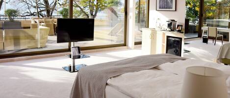 A modern hotel room with a large window, a bed, a desk, and a TV.