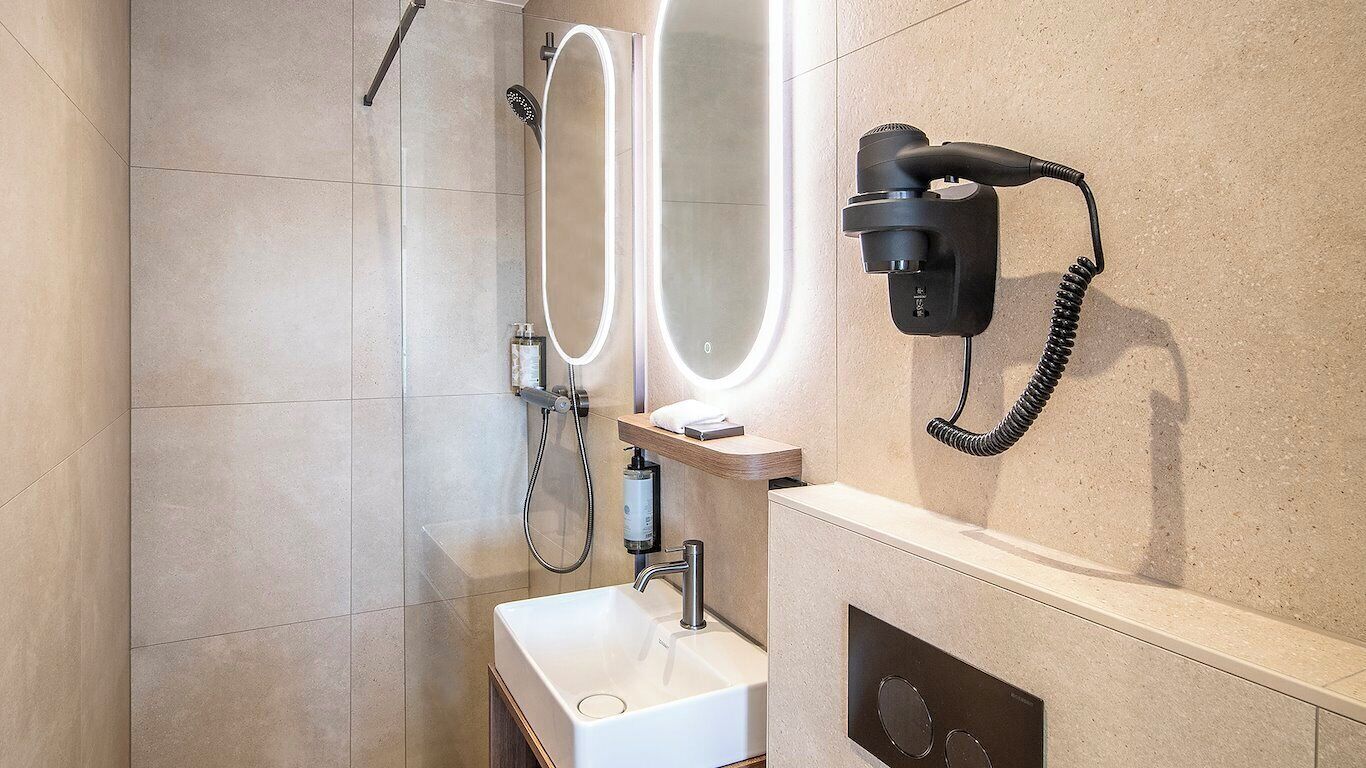 Une salle de bain moderne équipée d’un miroir, d’un sèche-cheveux, d’un lavabo et d’une douche.