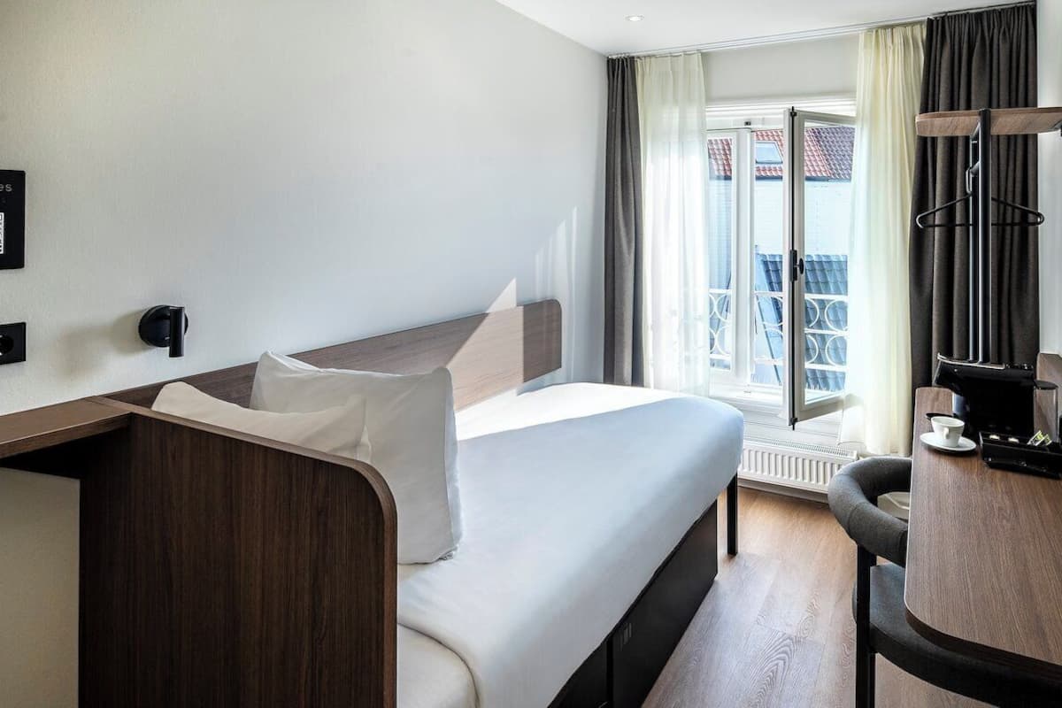 Habitación de hotel con cama, escritorio, silla, televisor y ventana con cortinas.
