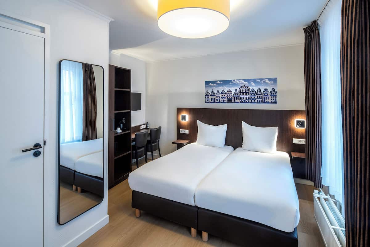 Habitación de hotel con una cama grande, un escritorio, una silla, un espejo y un cuadro en la pared.