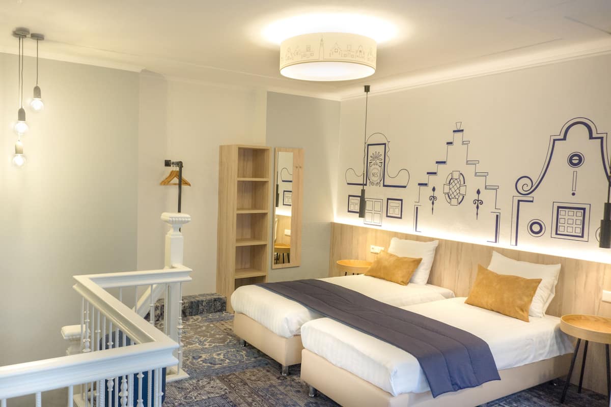 Habitación de hotel con escalera, dos camas, un armario de madera, un espejo y una pared con diseños decorativos.