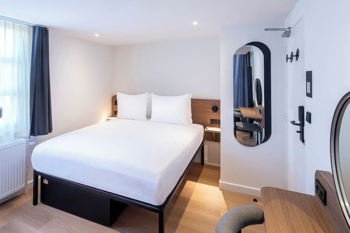 Una habitación de hotel moderna con una cama grande, una mesita de noche, un espejo y vistas al exterior.