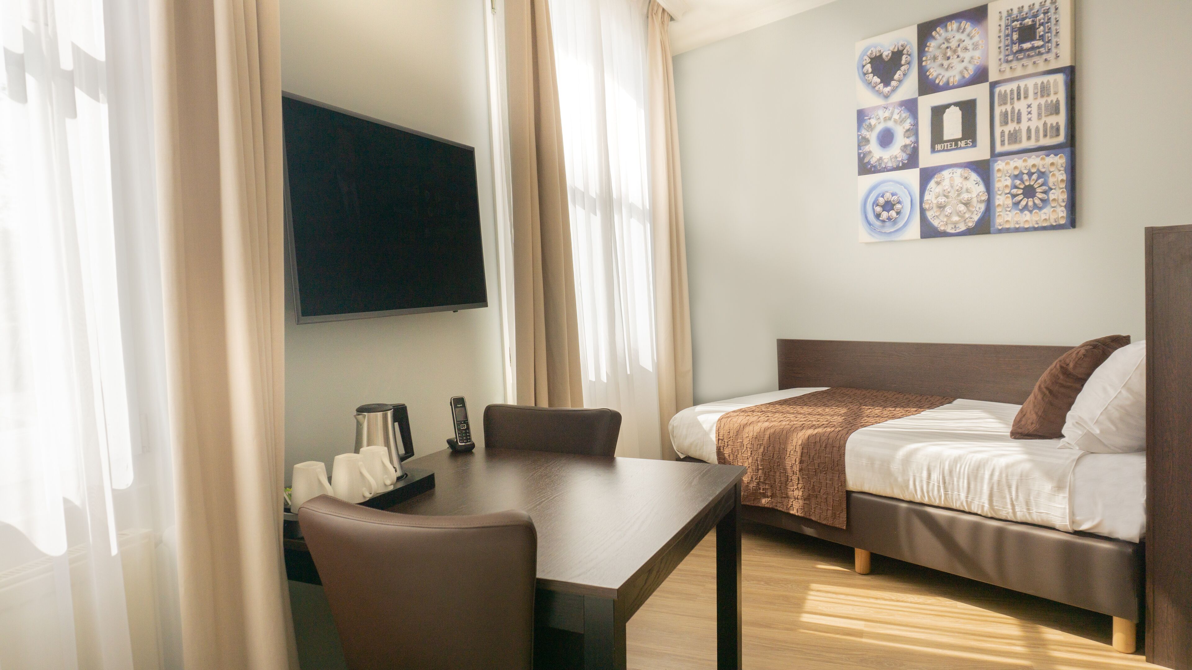 Een hotelkamer met een bed, een bureau, een stoel, een koffiezetapparaat en een tv aan de muur.
