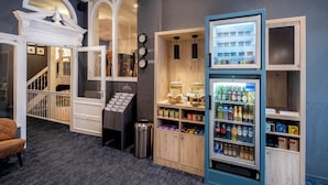 A hotel lobby with a staircase, a reception desk, a trash can, and a beverage refrigerator. - Hotel Nes Amsterdam (Amsterdam)
