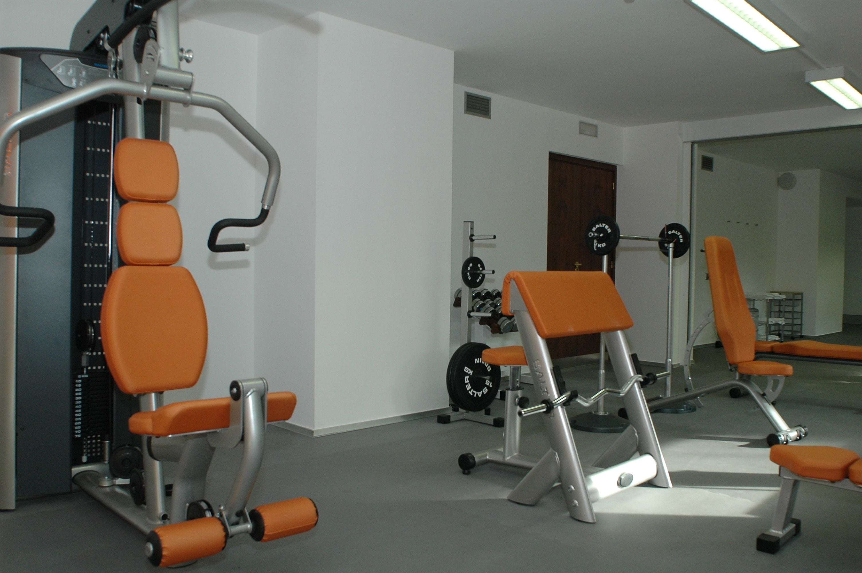 Une salle de sport avec des appareils orange, un support à poids et un miroir.