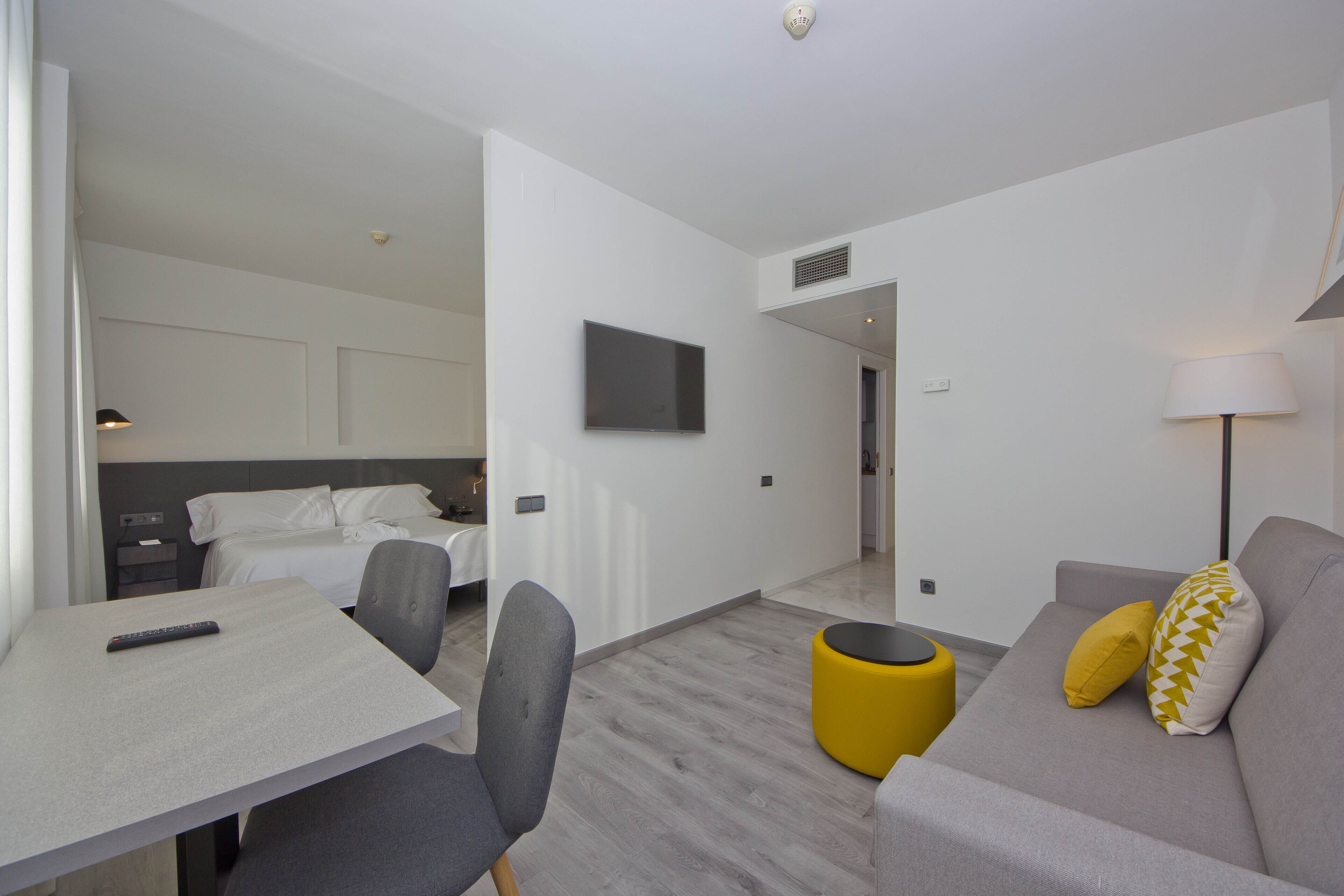 Una habitación de hotel moderna con una cama, un escritorio, un sofá y un televisor montado en la pared.