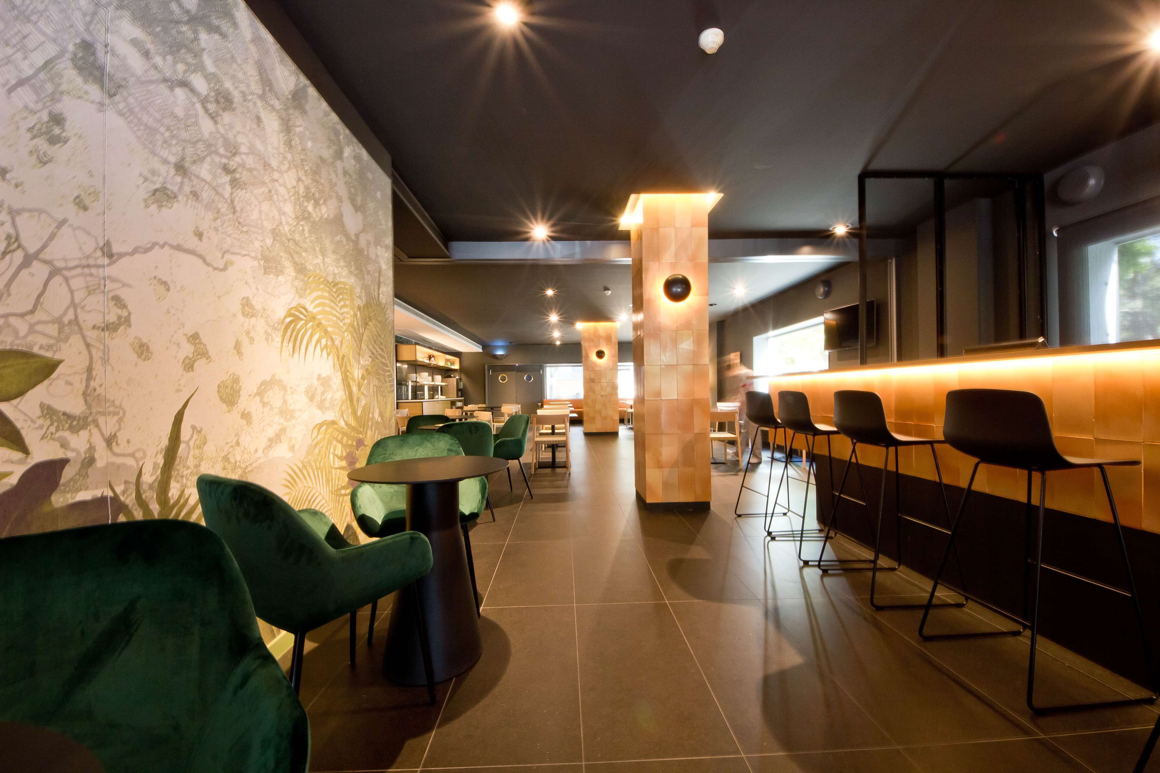 A modern interior with green upholstered chairs, a bar area, and a patterned wall.