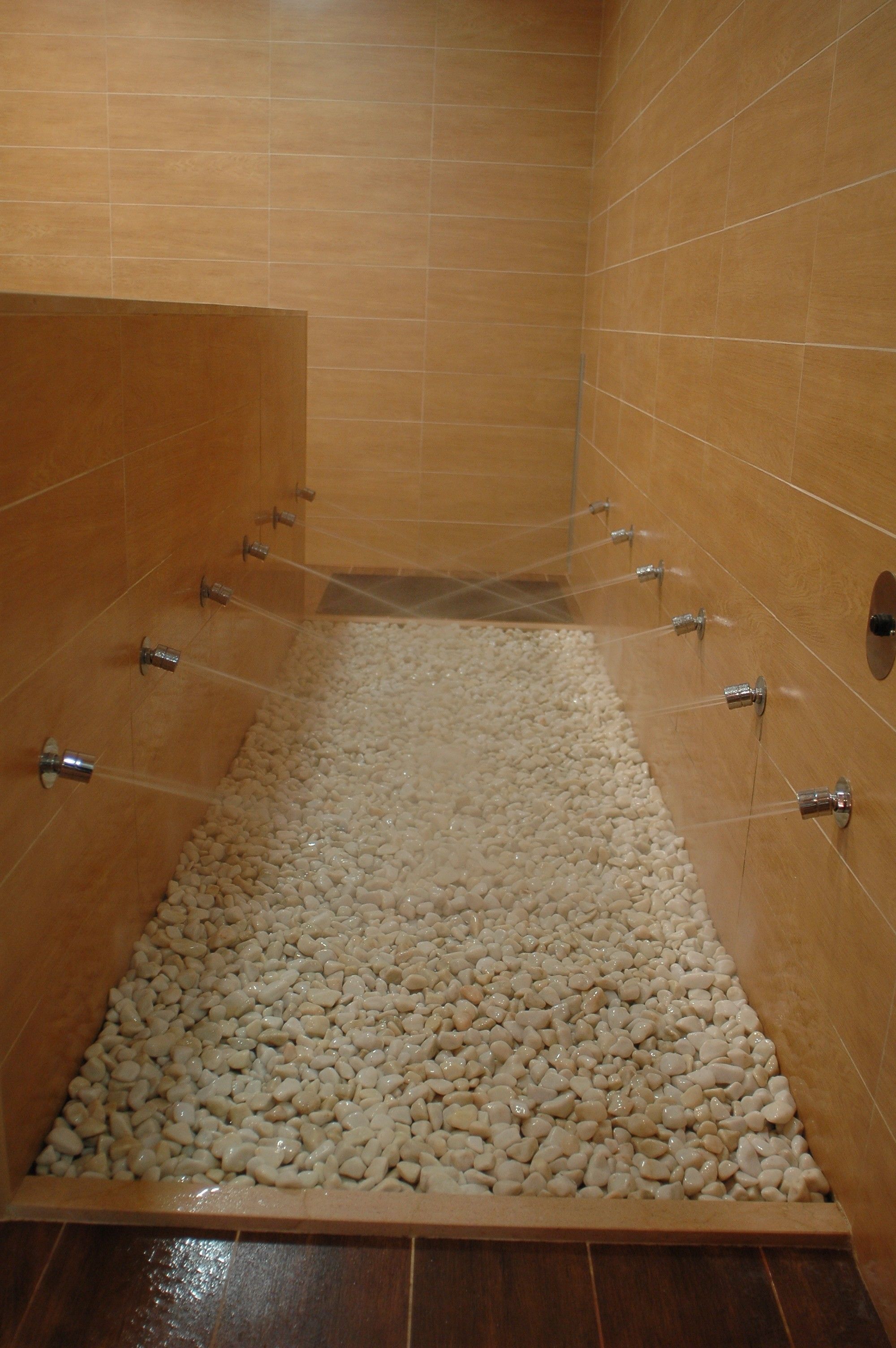 A shower with multiple nozzles, a pebble floor, and wooden walls.