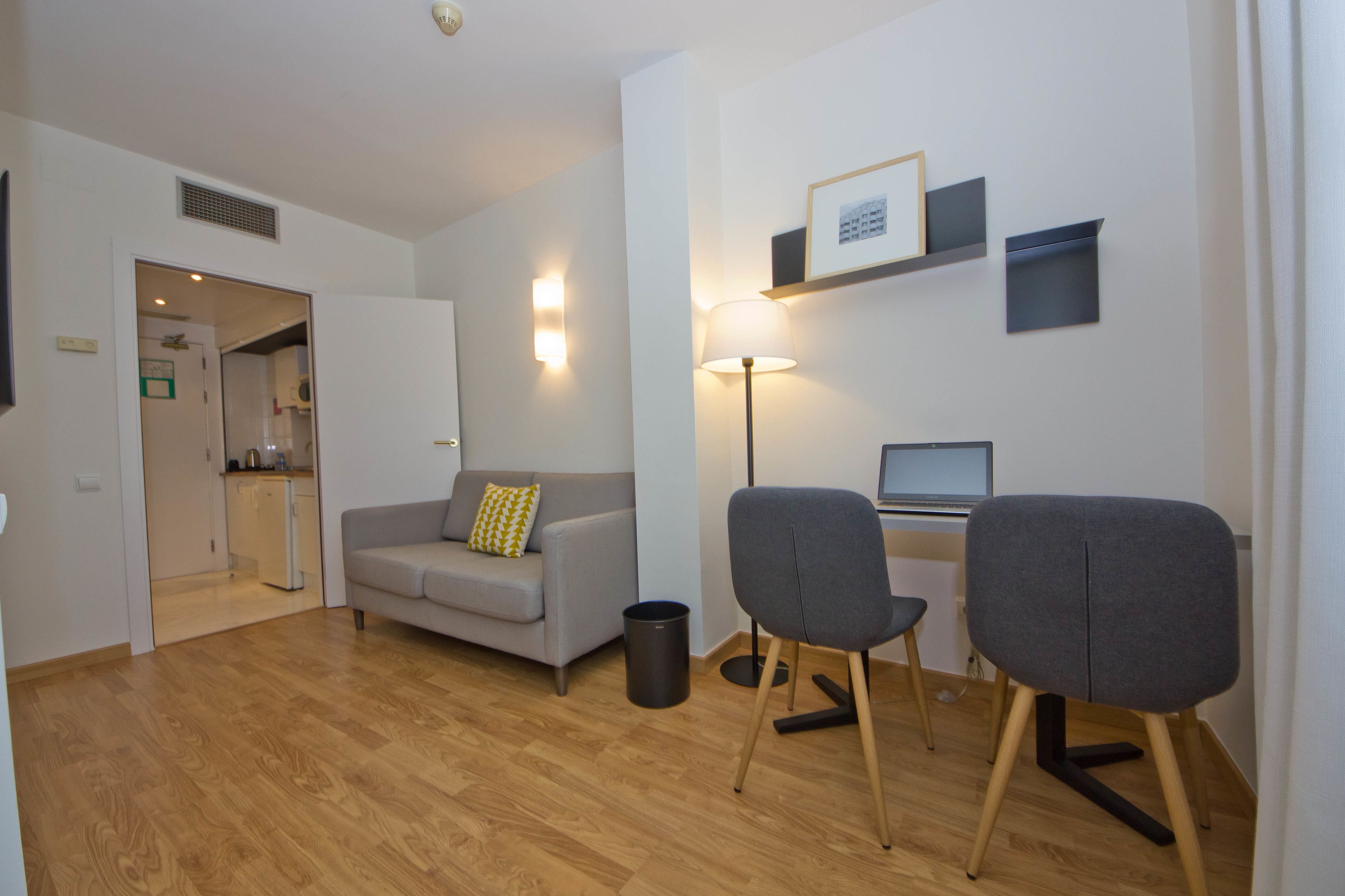 Ein modernes Wohnzimmer mit einem grauen Sofa, zwei grauen Sesseln, einer Stehlampe und einem Laptop auf einem Schreibtisch.