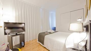 Una habitación de hotel con una cama, un televisor sobre un soporte, una mesita de noche con una lámpara y una botella de agua.