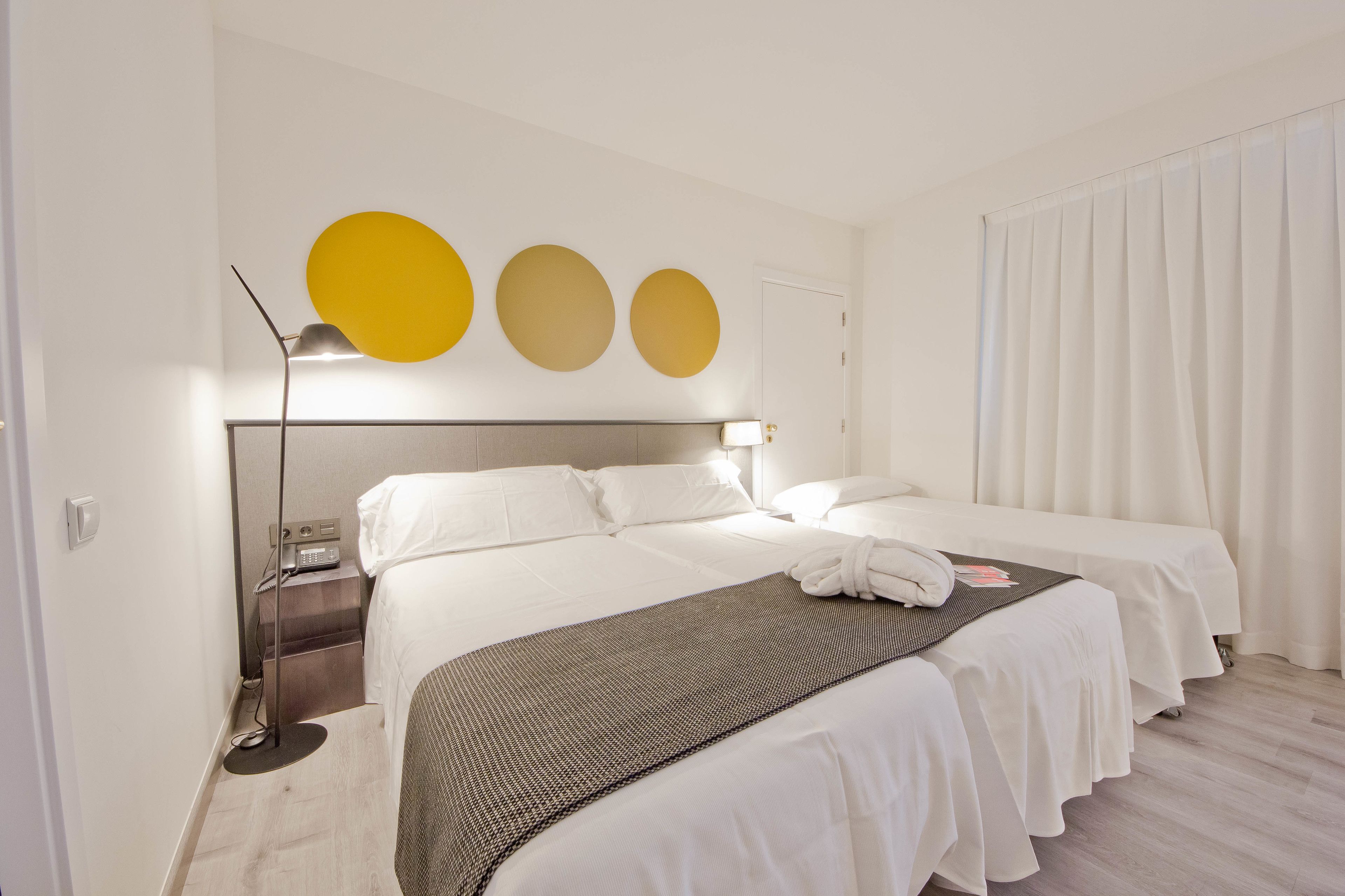 Ett hotellrum med en säng, sängbord, en lampa och en gardin.