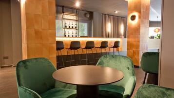 Un espace bar moderne avec un séparateur en bois, des chaises recouvertes de tissu vert et une table ronde.
