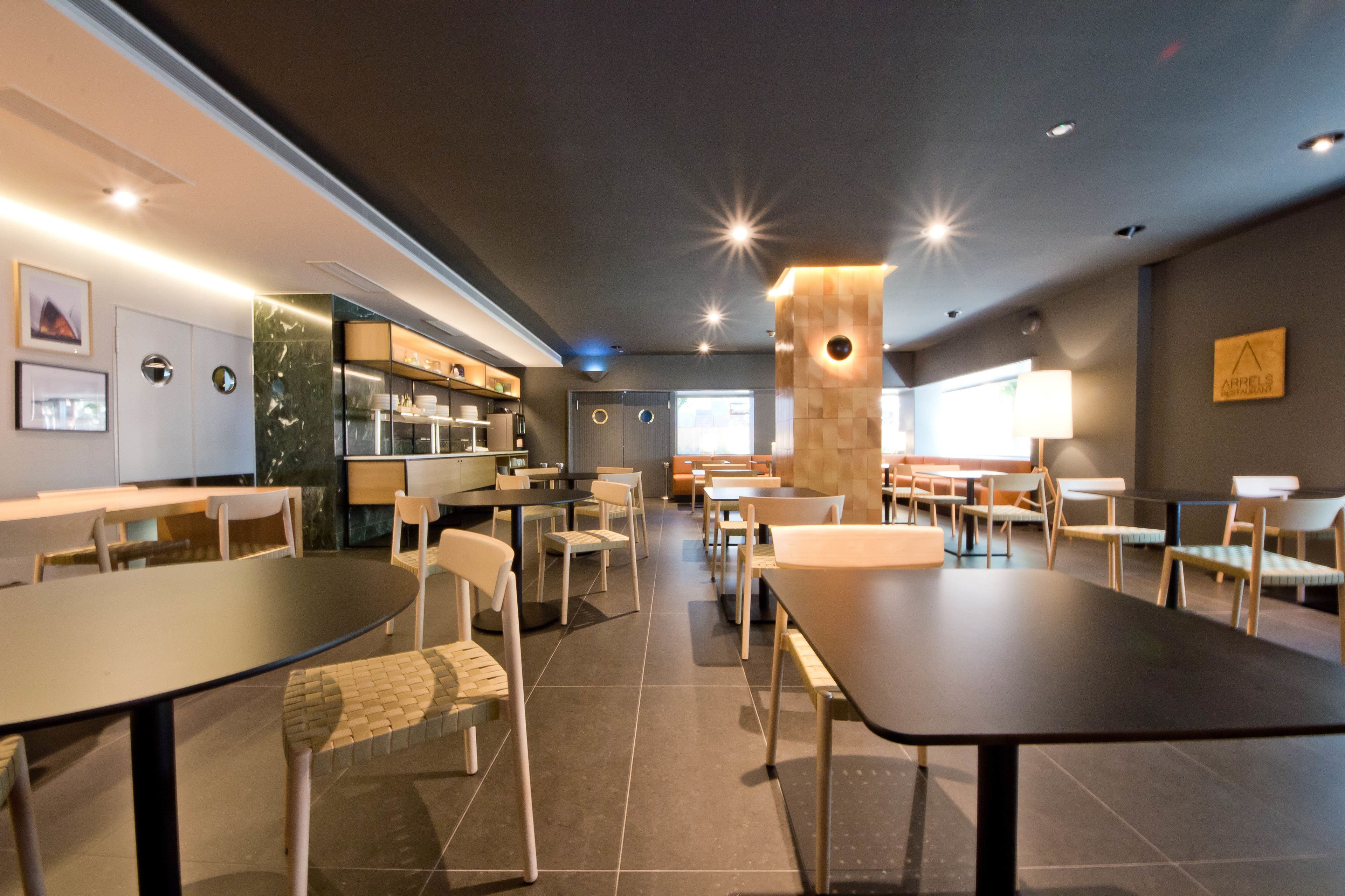 A modern restaurant with multiple dining tables and chairs, a kitchen area, and a bar.