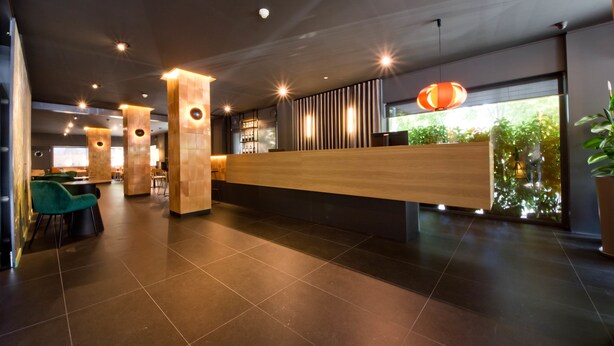 A modern reception area with a wooden reception desk, black-tiled flooring, and a large window with a view of greenery. - Aparthotel Atenea Valles (Granollers)
