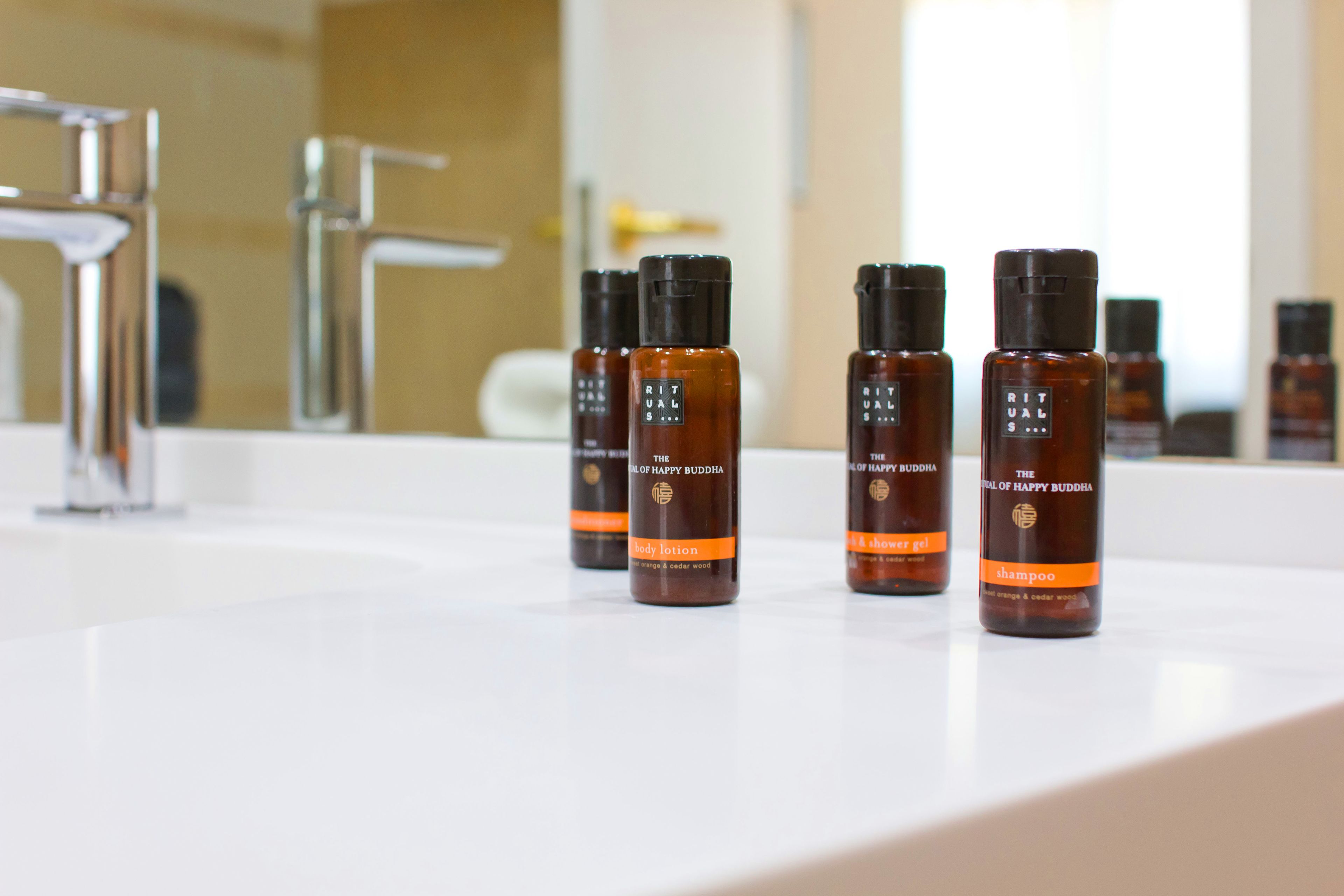 Un baño con un lavamanos blanco y cuatro botellas de loción corporal, gel de ducha y champú 'The Lotus of Happy Buddha'.