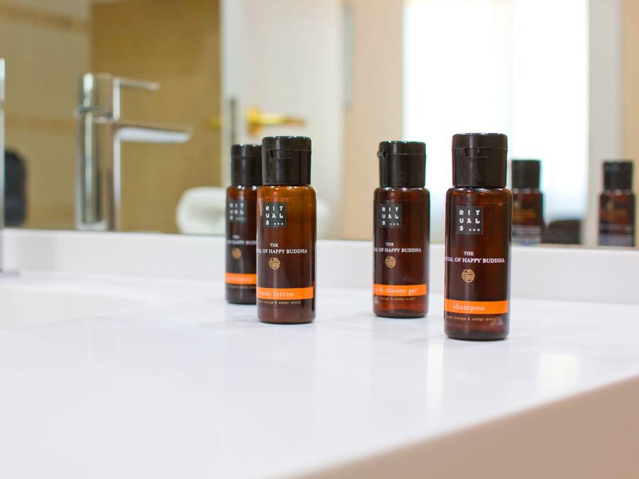 Un baño con un lavamanos blanco y cuatro botellas de loción corporal, gel de ducha y champú 'The Lotus of Happy Buddha'.