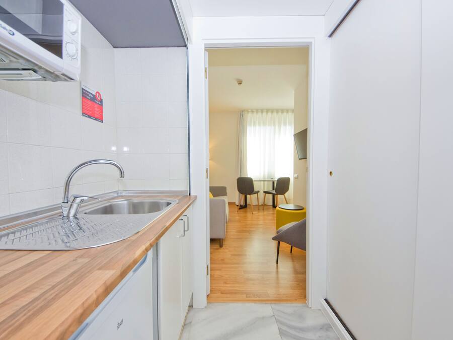 Et kompakt køkken med en moderne vask, en mikroovn og en lille spiseplads med bord og stole.