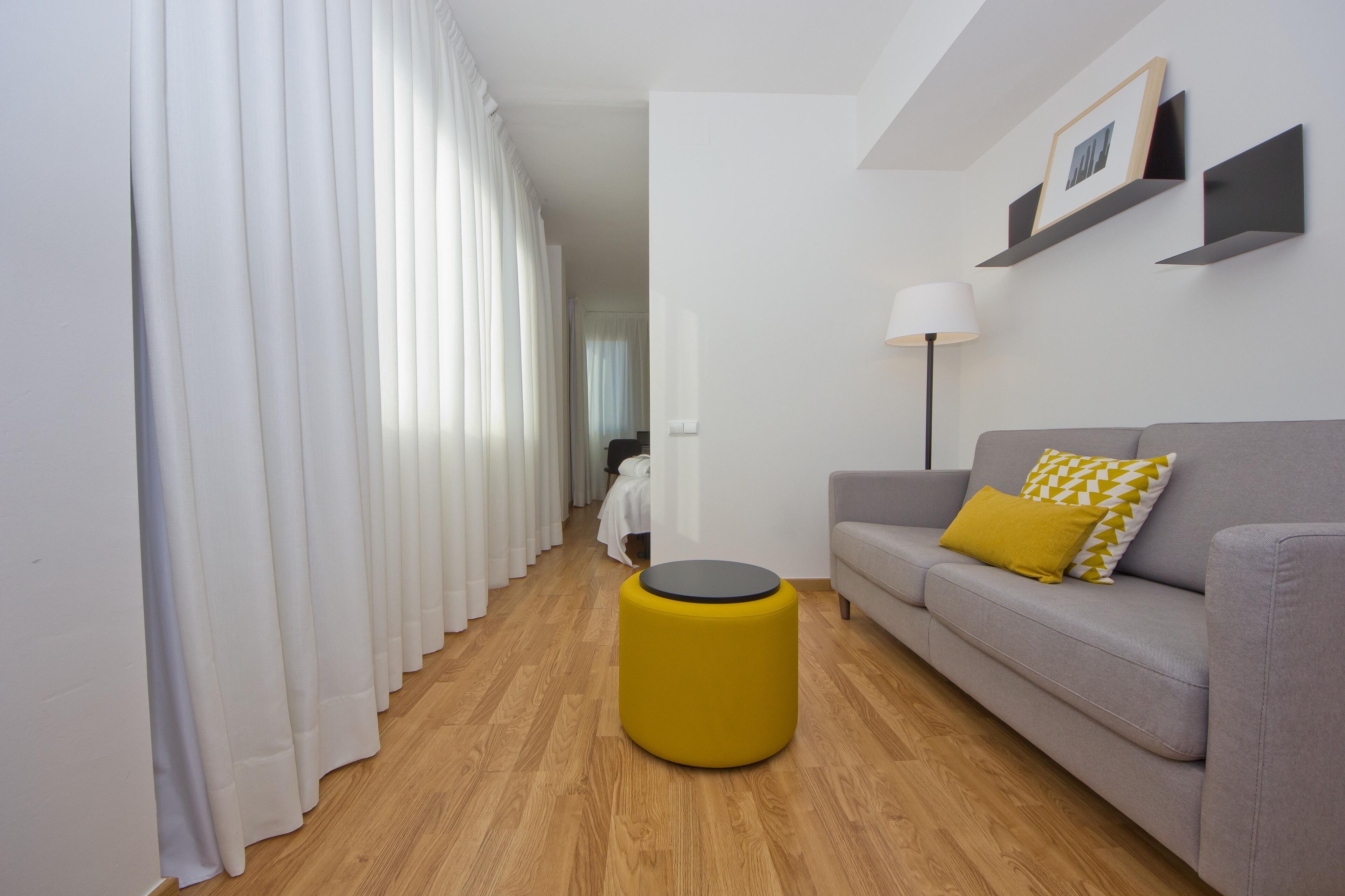 Een moderne woonkamer met een grijze bank, een geel voetenbankje en een witte vloer.