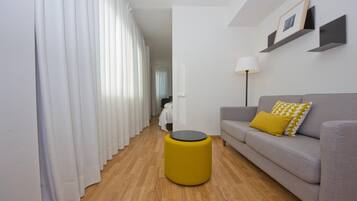 A modern living room with a grey sofa, a yellow ottoman, and a white floor.