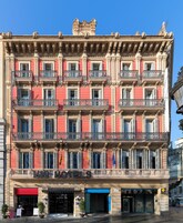A multi-story hotel with balconies, a red facade, and a ground-level entrance with signage.