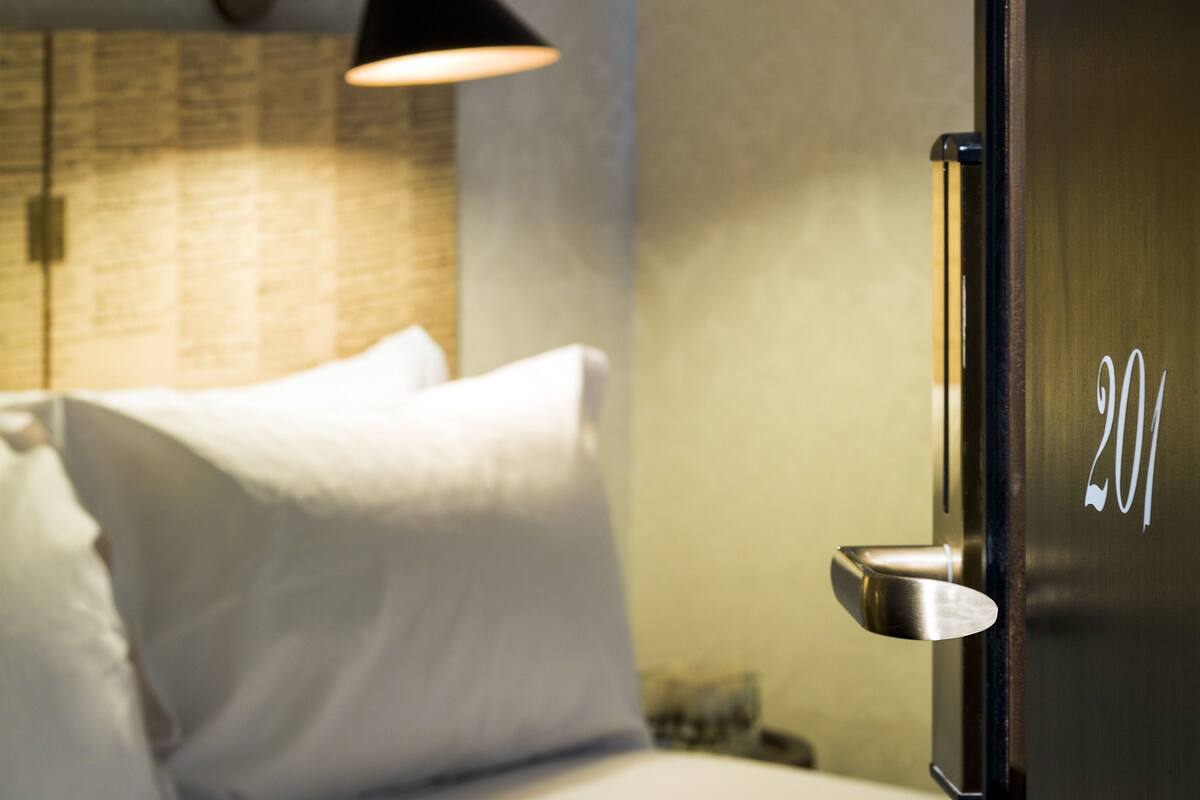 Une chambre d’hôtel avec un lit, une table de chevet, une lampe et une porte portant le numéro 201.